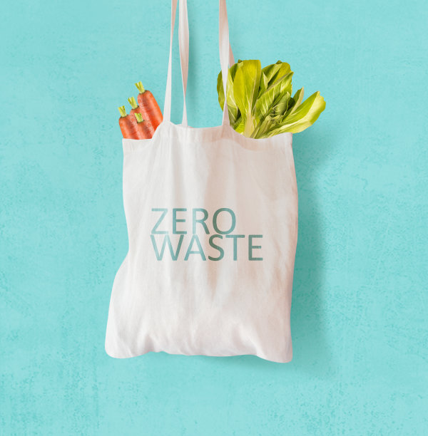 白色布袋上写着“零浪费”，里面装满了蔬菜，悬挂在明亮的蓝色背景前。图片下载