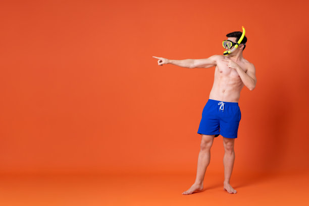 赤手空拳的男子，戴着潜水眼镜，穿着夏季短裤，用橙色背景指着复印空间图片下载