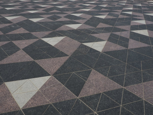 这个正方形铺着三角形的瓷砖。街上有灰色、白色、黑色的瓷砖。鹅卵石表面。现代设计的街道，大道，广场，购物中心。耐磨地板。图片下载