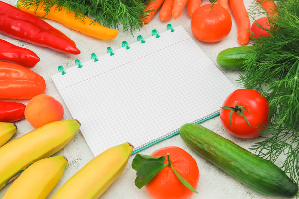 时令蔬菜和水果被摆放在大理石桌子上一个空的格子笔记本周围。图片下载
