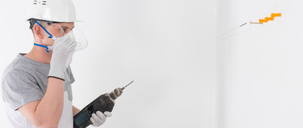 一个建筑工人戴着防护头盔和面罩，用打孔机在墙上打一个洞，用来固定家具，有一个地方可以题字图片下载