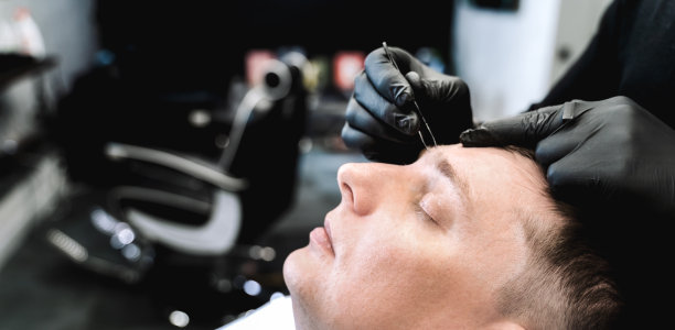 去理发店。用镊子拔眉毛，脱毛。理发师，美发师，发型师。顾客、顾客披着披肩坐在黑暗的男士美容院里图片下载