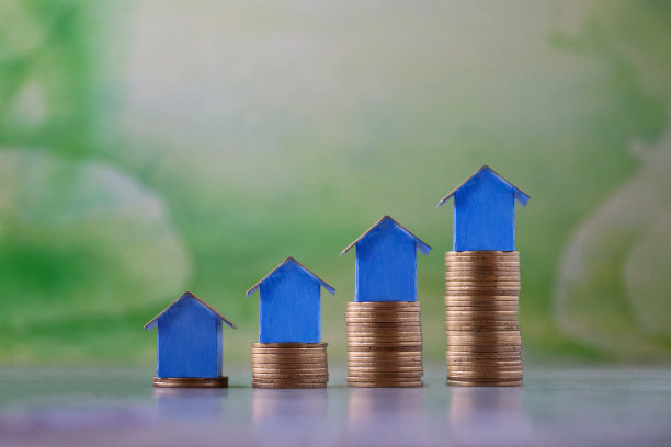 排蓝色纸板房子的特写图像，五颜六色的海滩小屋站在成堆的硬币上，重点放在前景，斑驳的绿色背景，家庭财务，房地产和假日储蓄概念图片下载