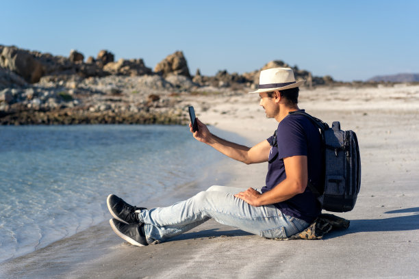 一个坐在沙滩上用智能手机自拍的男人图片下载