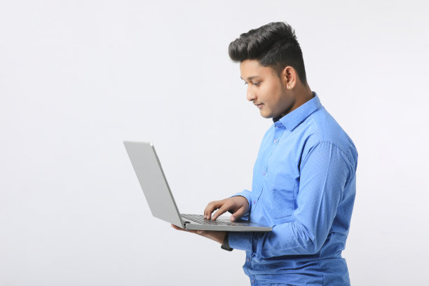 年轻的印度男子在白色背景上使用笔记本电脑。图片下载