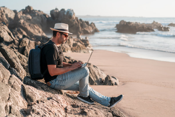 一个男人独自坐在沙滩上，拿着笔记本电脑远程办公或远程工作图片下载