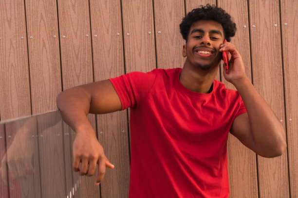 在木制背景上打电话的穿红色T恤的阿拉伯青年图片下载
