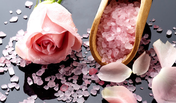 水疗和沐浴室内概念。粉红色的玫瑰花瓣和木勺在黑色的背景盐上图片下载