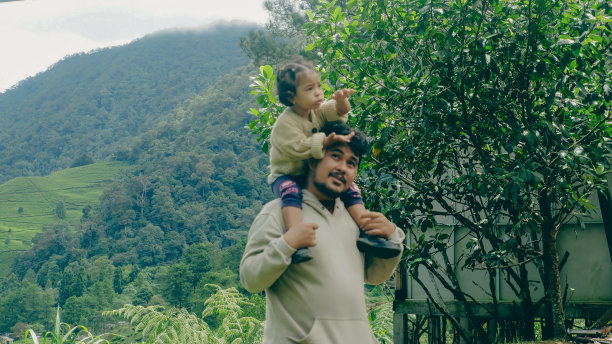 一个男人抱着他的女儿在一个绿色的公园里散步图片下载