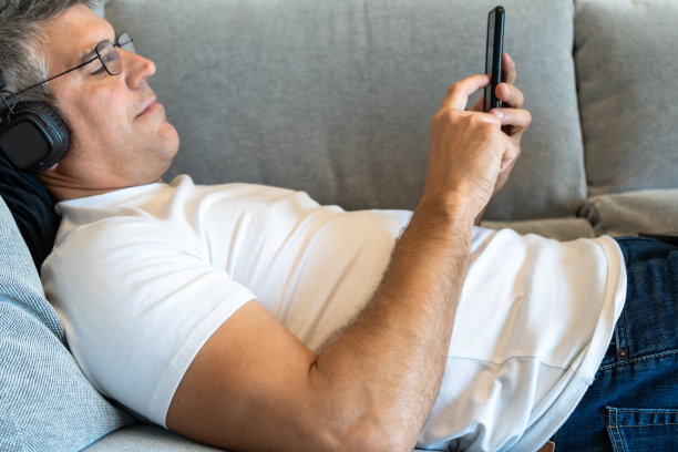 白发男子躺在沙发上，戴着耳机玩手机图片下载