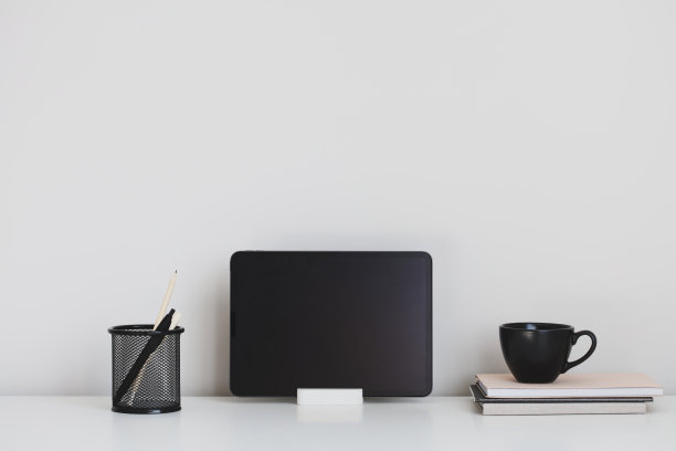 数码平板在支架上，一杯茶，办公文具在白色的桌子上。家庭办公室，现代工作空间。图片下载