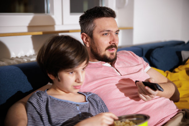 男孩吃着爆米花，和爸爸一起在家看电影图片下载