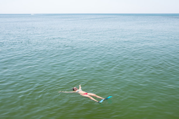 年轻女子仰面在海里游泳。图片下载