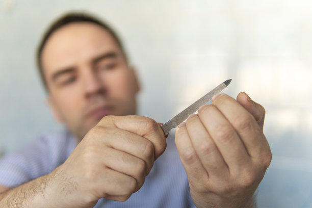 锯切指甲。这个男人正在用指甲锉剪指甲。护理指甲的概念，用指甲锉。注意你的外表和你自己。图片下载