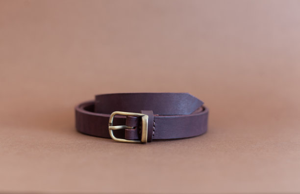 女人的腰带是茄子色的真皮，手工制作，躺在棕色的背景上。图片下载