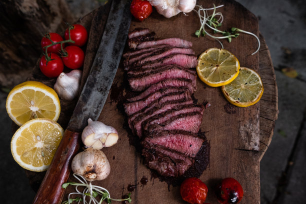 将烤牛肉放在切菜板上，配以盐腌蒜，番茄和柠檬图片下载
