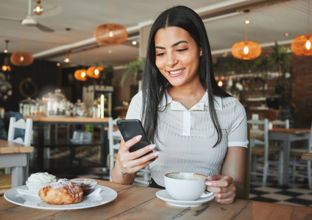 一名年轻女子在咖啡店里一边喝着咖啡一边用她的智能手机图片下载