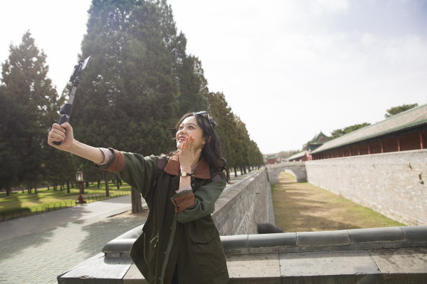 年轻的女导游手持自拍杆在智能手机上直播视频图片下载