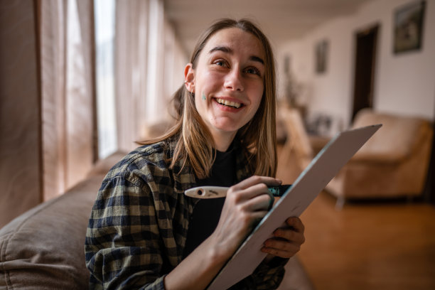 一个年轻美丽的白人女性艺术家坐在床沙发上画在画布上，拿着画笔艺术和创意专业或爱好概念真人前视图复制空间图片下载