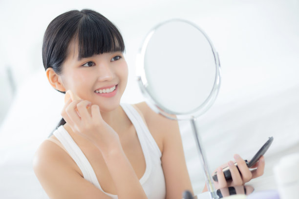 美丽年轻的亚洲女性在脸颊上涂粉扑化妆的化妆品镜子，美丽的女孩与皮肤脸和皱纹在卧室，美容为女性，护肤品的概念。图片下载