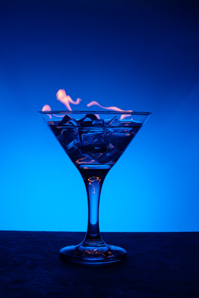 燃烧酒精饮料与冰块，蓝色渐变背景，垂直框架。在酒吧的桌子上燃烧鸡尾酒图片下载