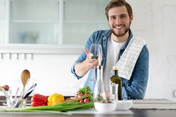 英俊的年轻人穿着便服，站在家里的厨房里喝酒。图片下载