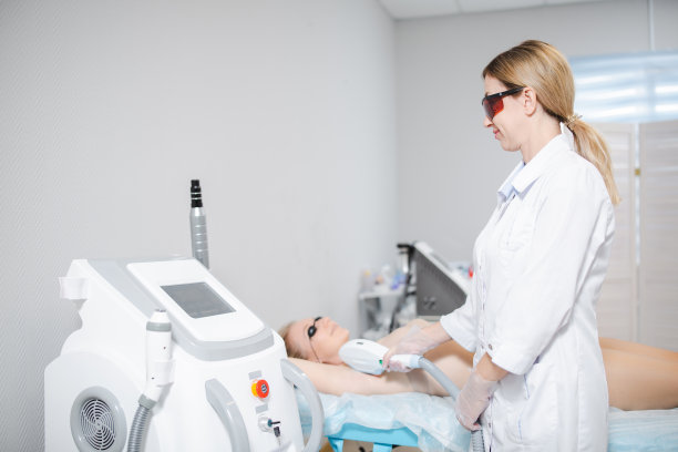 照片的一个现代美容设备和一个女皮肤科医生在保护眼镜进行手术激光脱毛的腋窝的一个年轻的女孩图片下载