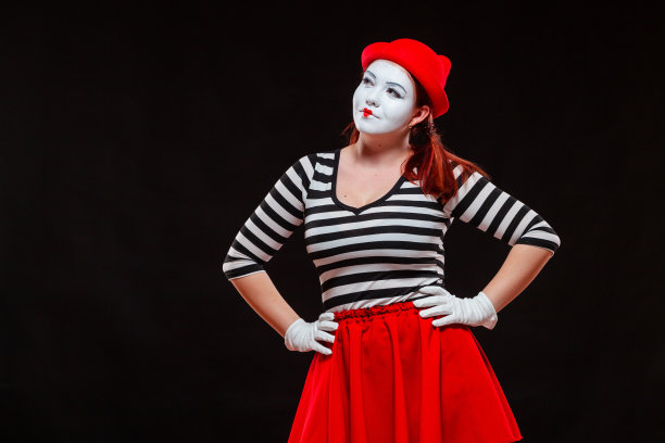 女哑剧艺术家表演的肖像，孤立在黑色背景上。穿着条纹衣服和红色裙子的女人双手叉腰站在那里图片下载