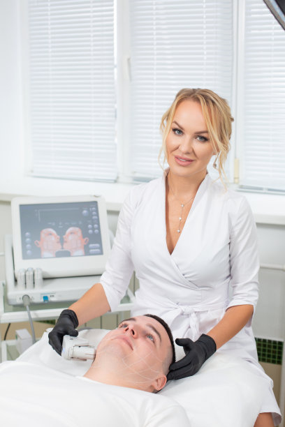 照片是一个年轻美丽的美容师进行激光面部毛发去除程序与现代设备的一个男人躺在沙发在美容办公室图片下载