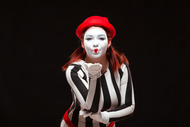 女哑剧艺术家表演的肖像，孤立在黑色背景上。一名身着条纹裙的女子摆出飞吻姿势图片下载