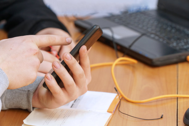 学生或自由职业者在笔记本电脑前用手指着手机屏幕图片下载