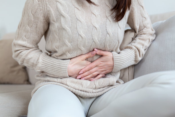 客厅里躺在沙发上的女人看起来病了。美丽的年轻女子躺在床上，手放在肚子上。月经期间卧床胃痛的妇女图片下载