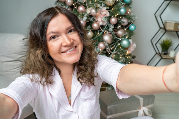 年轻漂亮的女人长头发，穿着舒适的睡衣，坐在地板上自拍，家里有圣诞树图片下载