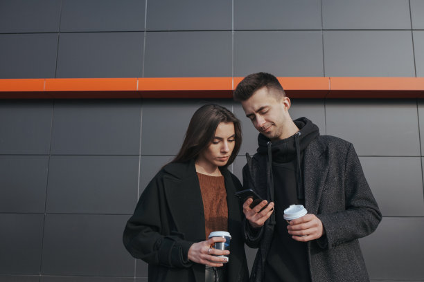 一对年轻的情侣在黑色工业背景下喝着咖啡，调查男友的手机图片下载