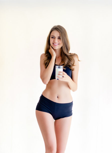年轻女子美丽苗条的身材微笑着拿着一杯牛奶，穿着黑色的连衣裙，锻炼身体图片下载