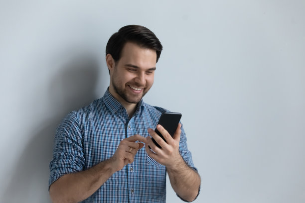 一个微笑的家伙拿着智能手机在灰色的工作室背景上摆姿势图片下载