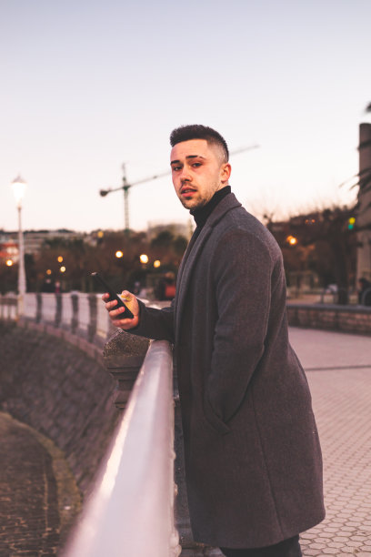 日落时分，在多诺斯塔-圣塞巴斯蒂安海滨散步，一名年轻的白人男子在使用智能手机。图片下载