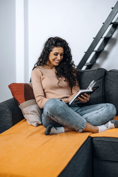 年轻漂亮的女人在沙发上看书。图片下载