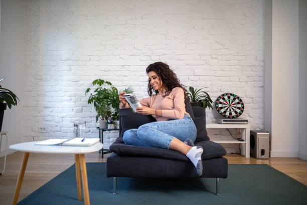 年轻女子坐在舒适的扶手椅和打开的书在室内。图片下载