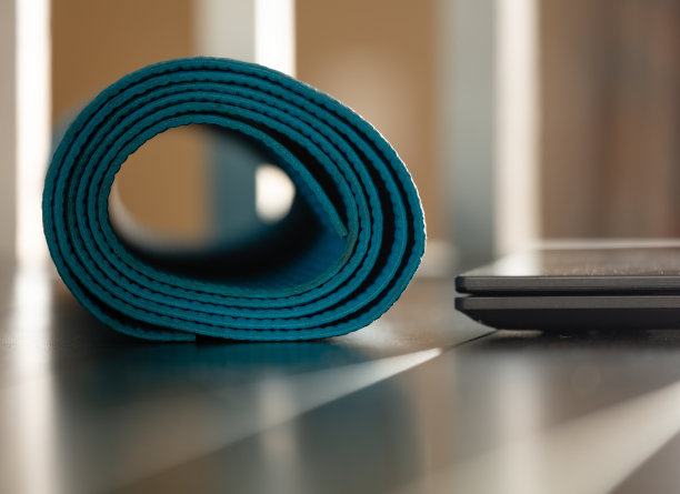 笔记本电脑旁边卷起的瑜伽垫的特写图片下载