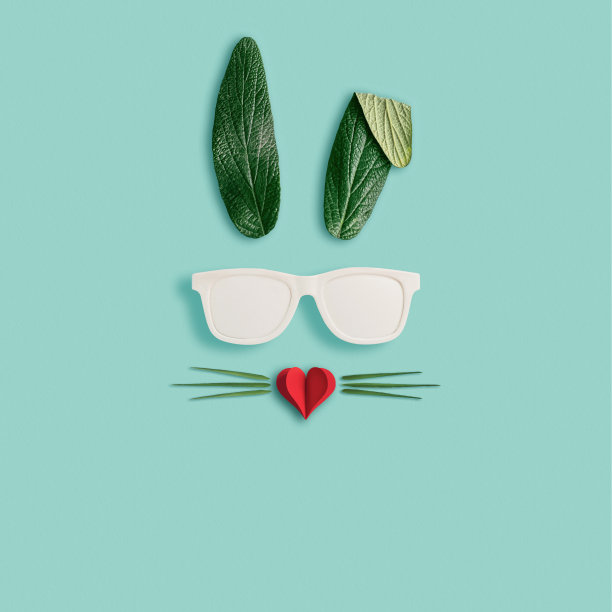 快乐复活节最小概念。兔子兔子脸由天然绿色的叶子与太阳镜和红色的心在柔和的蓝色背景。平的。图片下载