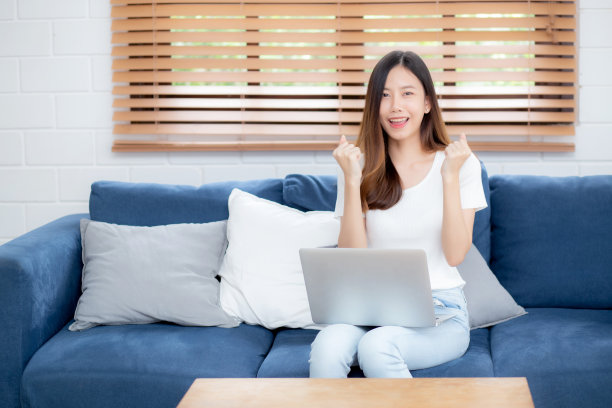 年轻的亚洲商业女性微笑着在家里用笔记本电脑在线工作，在客厅的沙发上上网，自由职业女孩使用笔记本电脑在沙发上舒适，新常态，生活方式的概念。图片下载