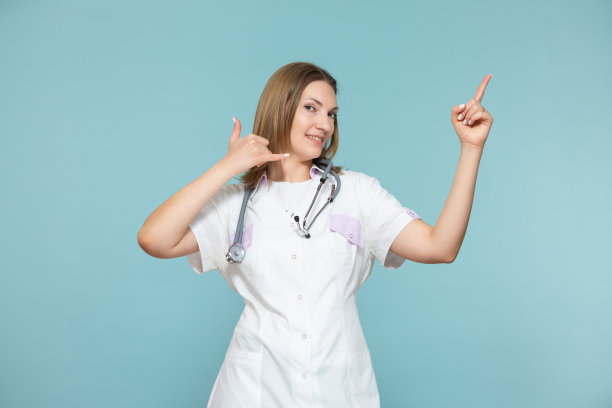 一名女医生在蓝色背景上展示一个电话符号，并用手指着广告方法或电话号码。复制粘贴。医疗保健的概念图片下载