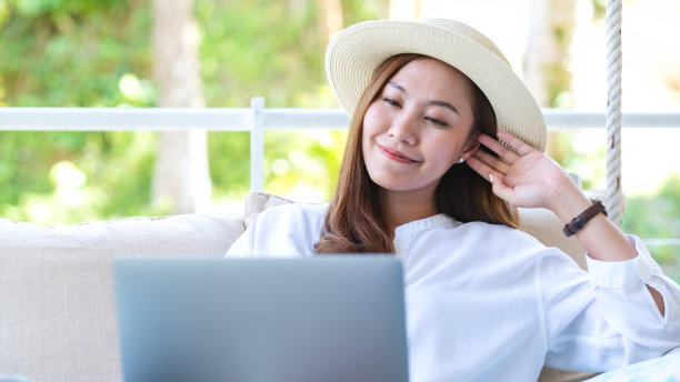 肖像的一个美丽的年轻亚洲女子使用笔记本电脑远程工作或在线学习，而坐在秋千沙发上图片下载