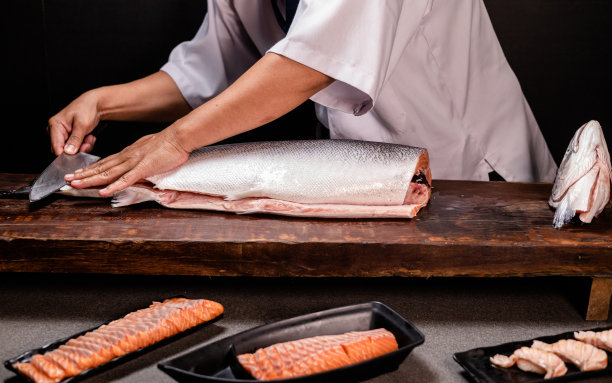 厨师的手握着新鲜的三文鱼。厨师准备日本食物的特写镜头。日本厨师在餐厅做寿司。厨师在木板上制作传统的日本寿司。图片下载