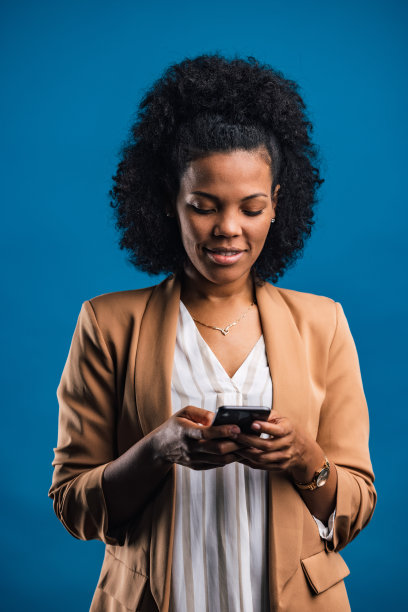 一个非洲女人在摄影棚里，用手机摆姿势。图片下载