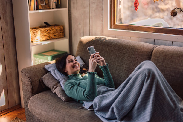 放松的女人躺在床上，用手机，微笑着。图片下载