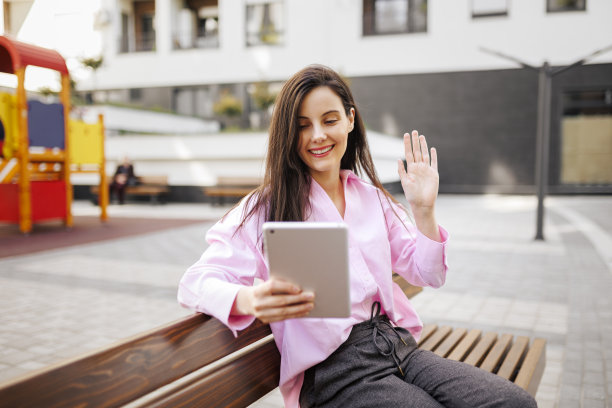 美丽的女人坐在公园的长椅上，用她的数码平板电脑，看报纸和视频电话图片下载