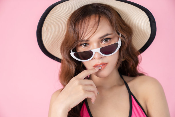 快乐迷人的年轻漂亮的女人穿着泳衣，戴着太阳镜和帽子。时尚人像照片优雅漂亮的女孩孤立在粉红色的背景。夏天和美的概念。图片下载