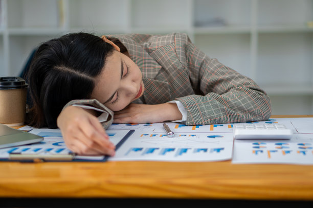 有吸引力的亚洲女商人睡觉，昏昏欲睡，或在她的办公桌上午睡。一个厌倦了办公室里的财务档案的会计。桌上放着财务图表和笔记本电脑图片下载